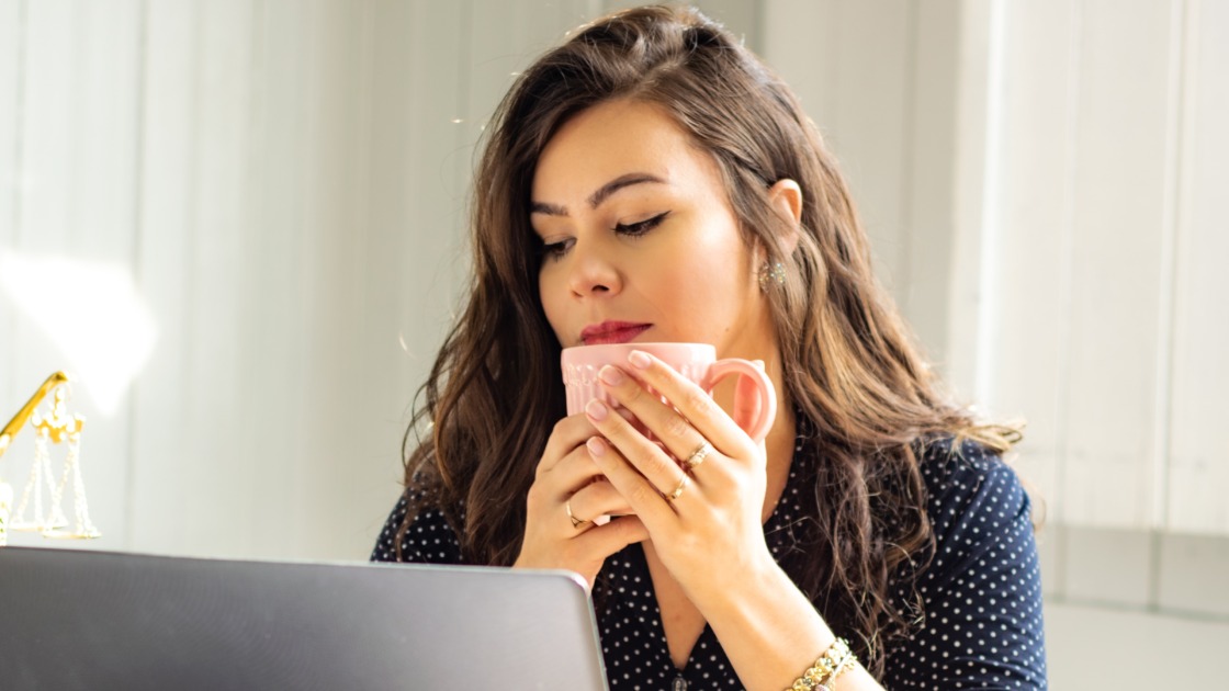 A virtual assistant is looking at the computer while holding a cup of coffee.