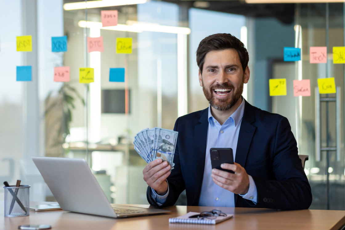 Businessman holding cash and phone in modern office with sticky notes on glass