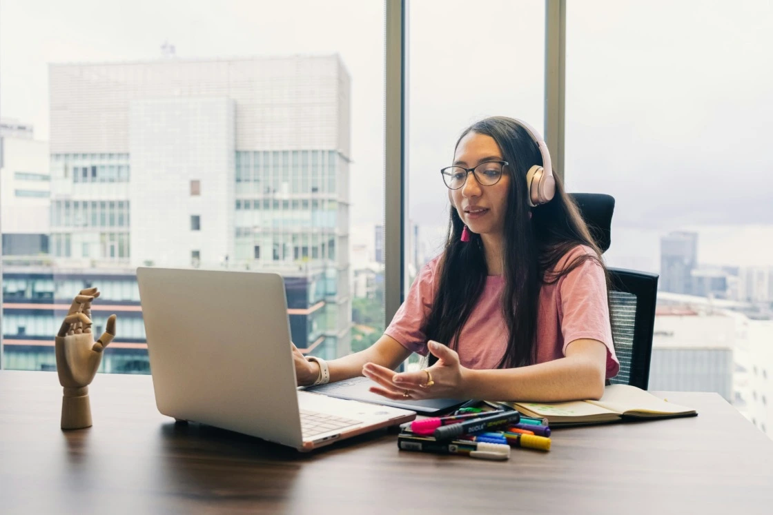 Joven profesional trabajando desde su laptop con audífonos, aprendiendo y aplicando habilidades digitales en un entorno laboral moderno.
