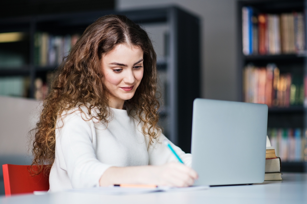 Studentka w bibliotece przed laptopem sprawdza, jak pogodzić studia i pracę