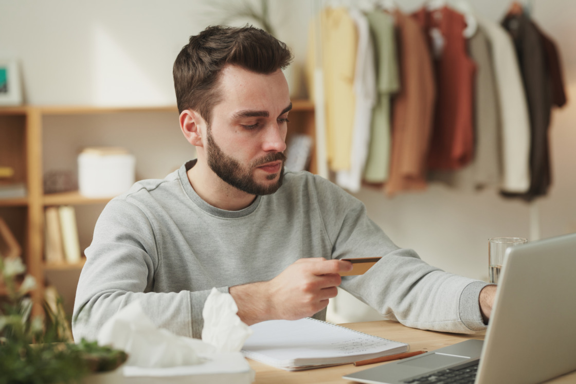 Płynność finansowa freelancera krok po kroku Młody freelancer pracujący przy komputerze sprawdza stan swojej karty kredytowej i rady o tym, jak zadbać o płynność finansową na freelansie
